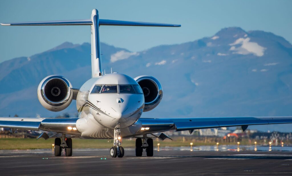 Private luxury business jet parked on airport runway with mountains in the background